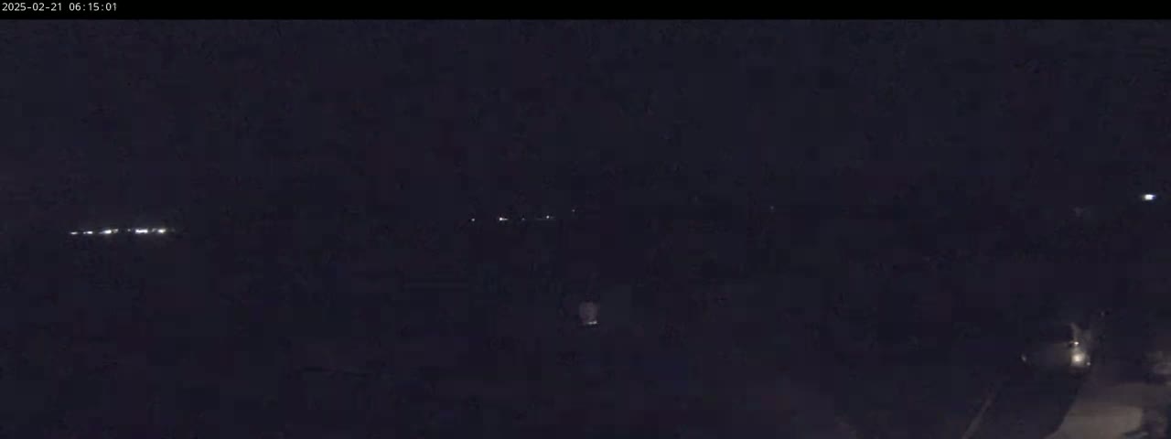A nighttime, low-light view shows a dark landscape with a few distant lights and a single brighter light closer to the viewer.