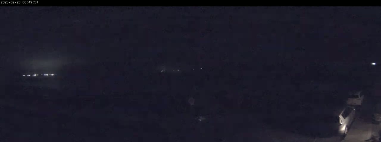 A dark, nighttime scene shows a few faint lights in the distance and two vehicles parked near the bottom right corner.