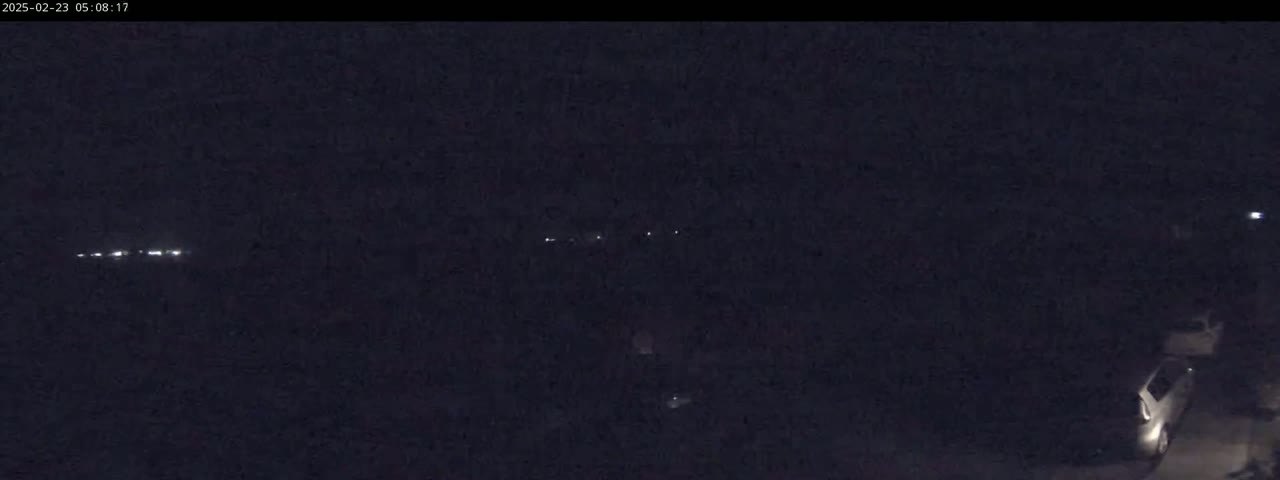 A dark nighttime scene shows a distant line of headlights and a single car parked in the lower right corner.