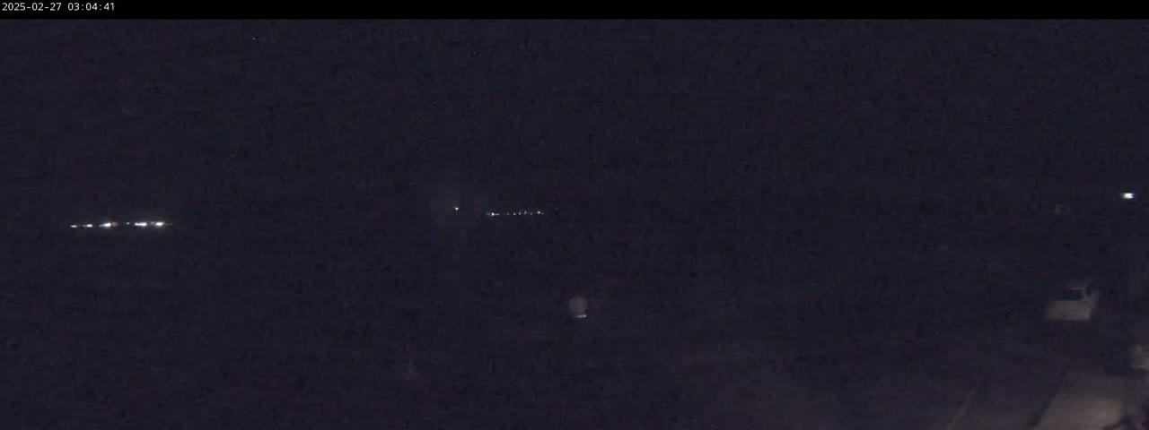 A nighttime, long-distance view shows a line of distant lights, possibly headlights from vehicles on a road.