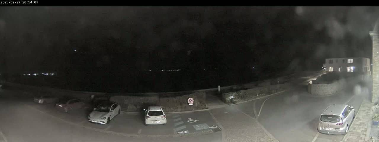 A nighttime view of a parking lot with several cars parked, under a dark, possibly rainy sky.