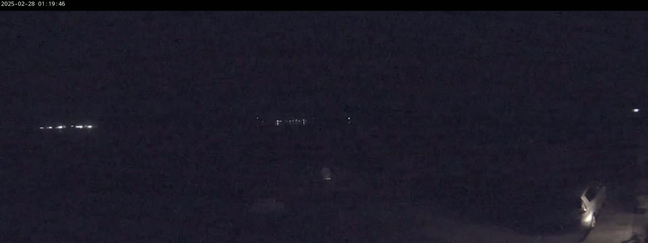 A dark, nighttime scene shows a few distant headlights on a road and a vehicle parked at the bottom right.