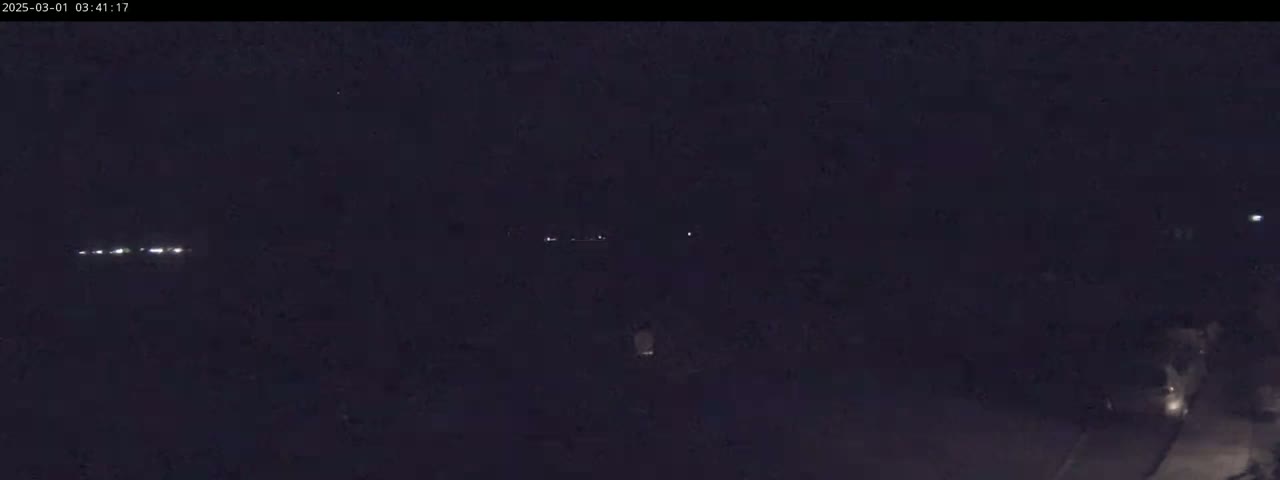 A nighttime, dark image shows a few faint lights in the distance, possibly from vehicles, against a mostly black background.