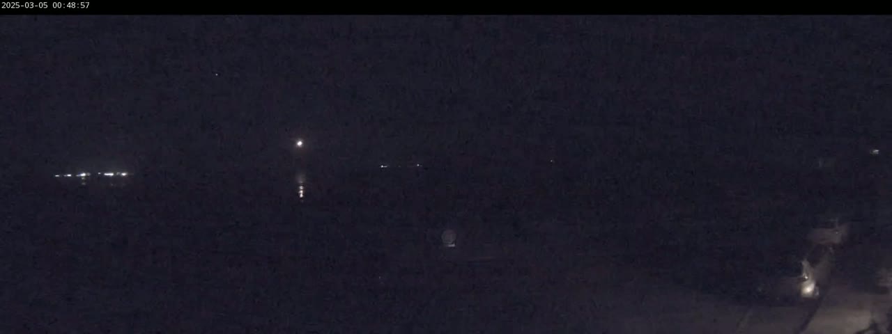 A dark, nighttime scene shows faint lights in the distance across a body of water under a clear sky.
