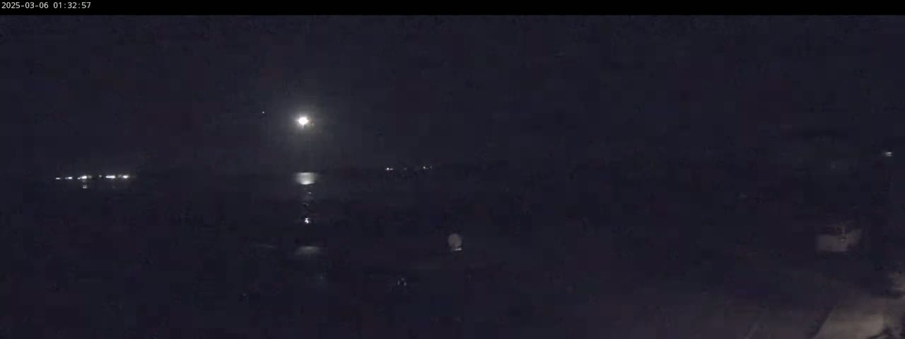 A nighttime long shot shows a bright moon illuminating a dark body of water and dimly lit shoreline.