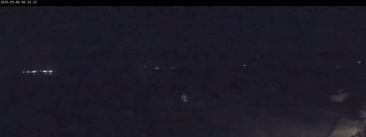 A dark, nighttime scene shows a few faint lights in the distance, possibly from vehicles or buildings.