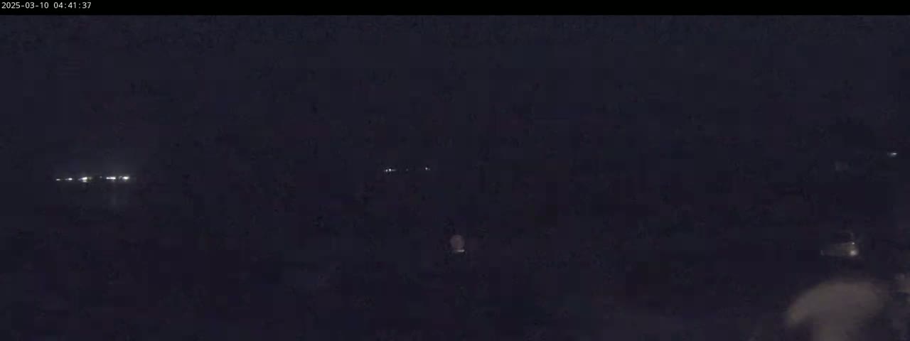 A nighttime, dark outdoor scene shows faint lights in the distance.