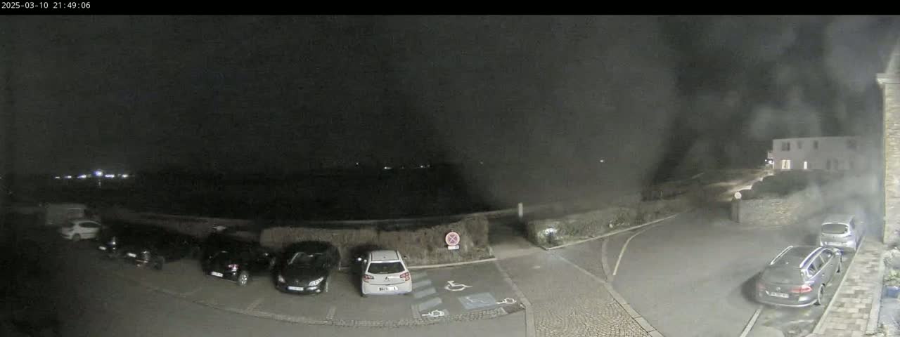 A nighttime view of a parking lot with several cars parked, under a hazy, dark sky.