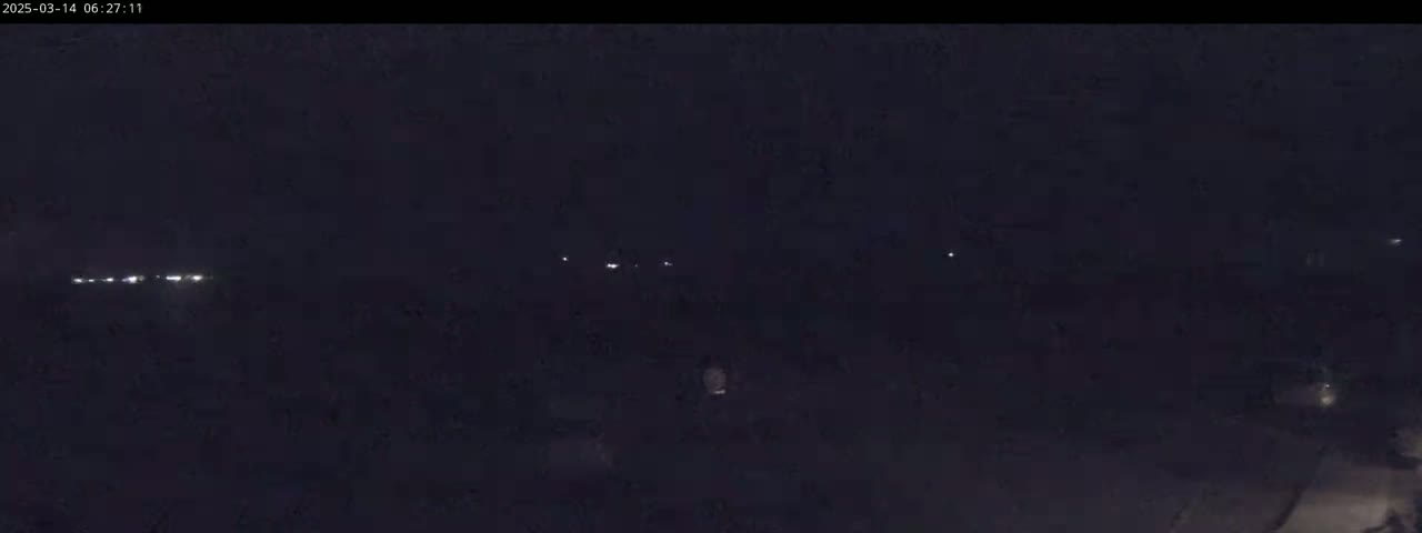A dark, nighttime scene shows a line of distant lights, possibly from a road or buildings, under a clear, dark sky.