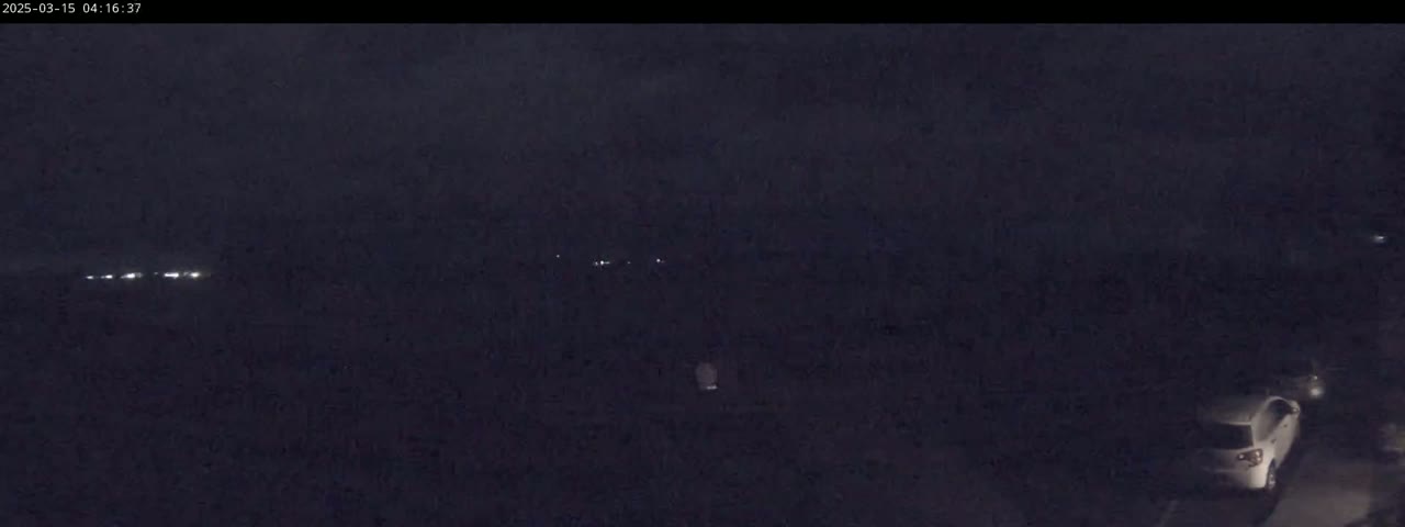 A dark, nighttime scene shows a few distant lights and a white car parked near the bottom of the frame.
