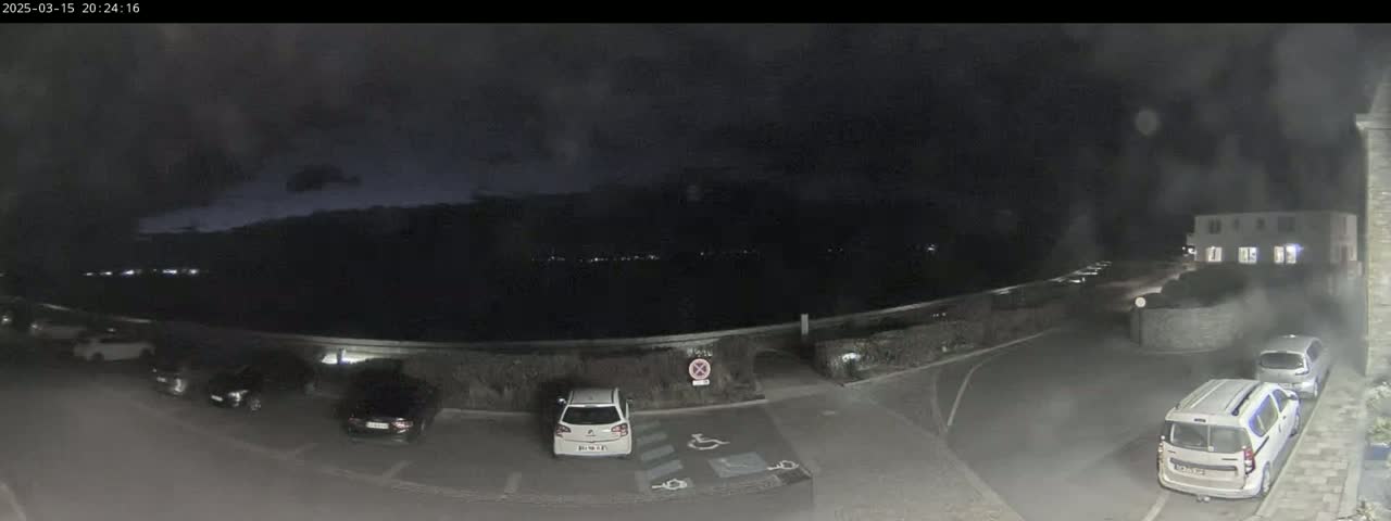 A nighttime parking lot with several cars, overlooked by a building, under a dark, cloudy sky.