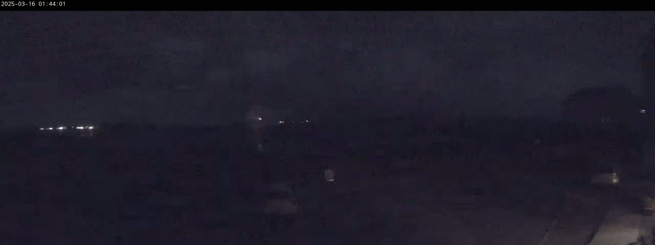 A dark, nighttime scene shows a few distant lights and shadowy figures in the foreground under a cloudy sky.