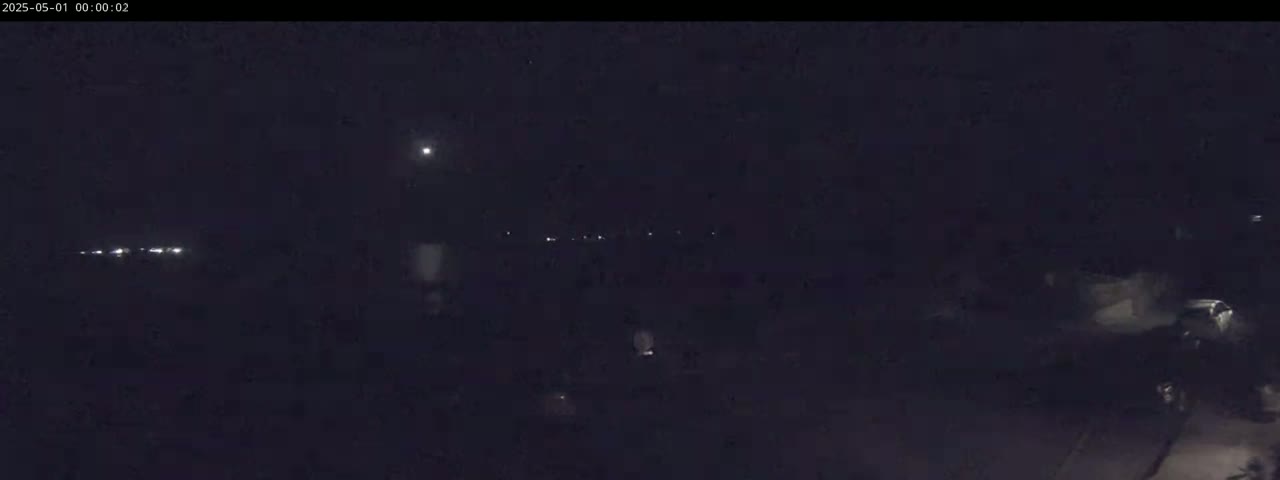 A dark, nighttime scene shows a few distant lights and some indistinct shapes in the foreground under a clear, moonlit sky.
