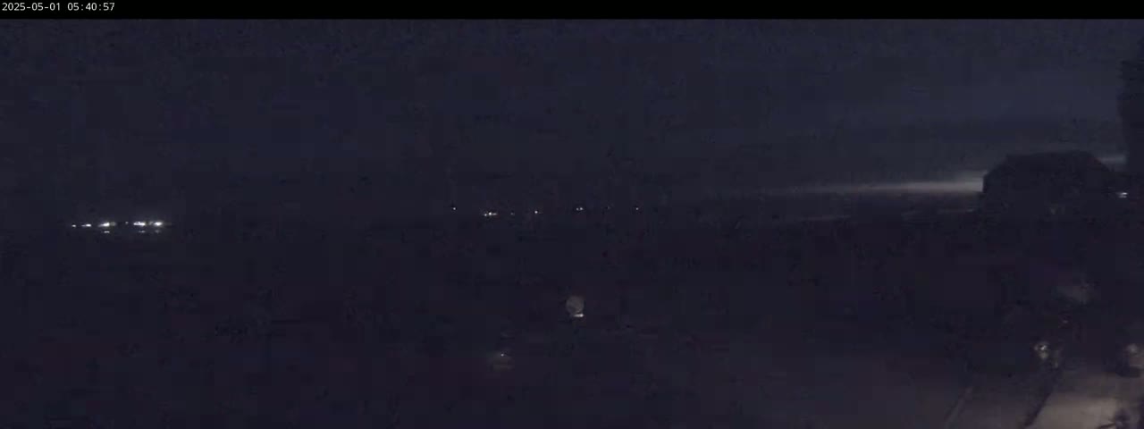 A dark, nighttime scene shows a few distant lights in the far background, and a mostly obscured structure to the right.