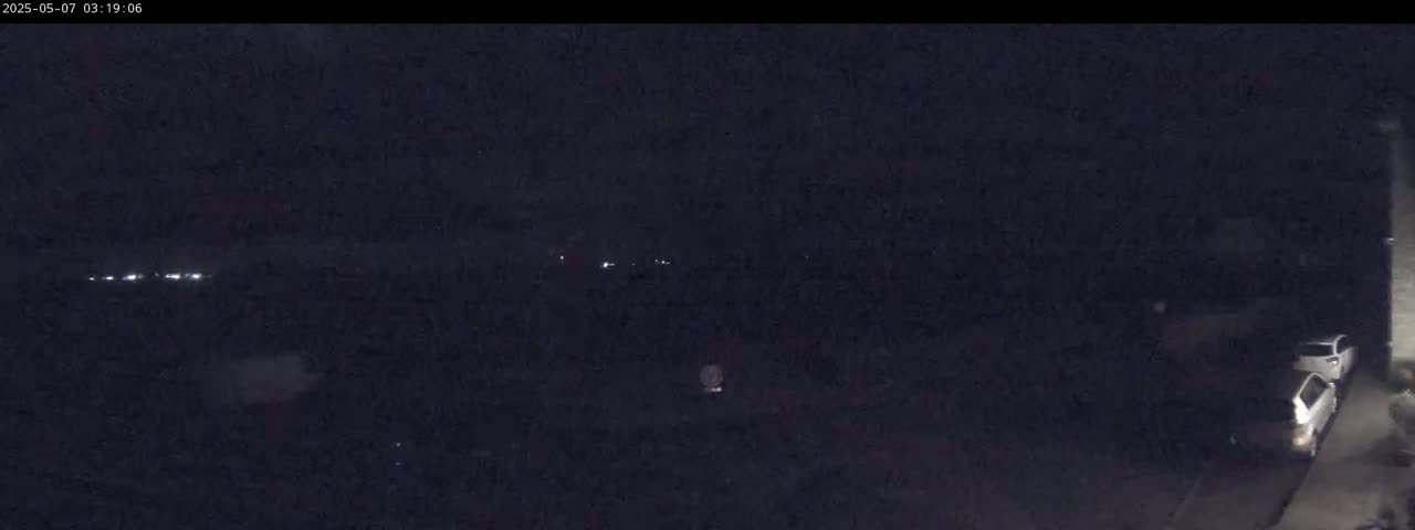 A nighttime outdoor scene shows a few distant lights and two parked cars in a dark, possibly residential area.