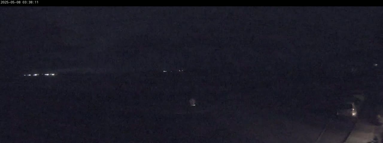 A dark, nighttime scene shows a few distant lights in the horizon under a mostly clear sky.