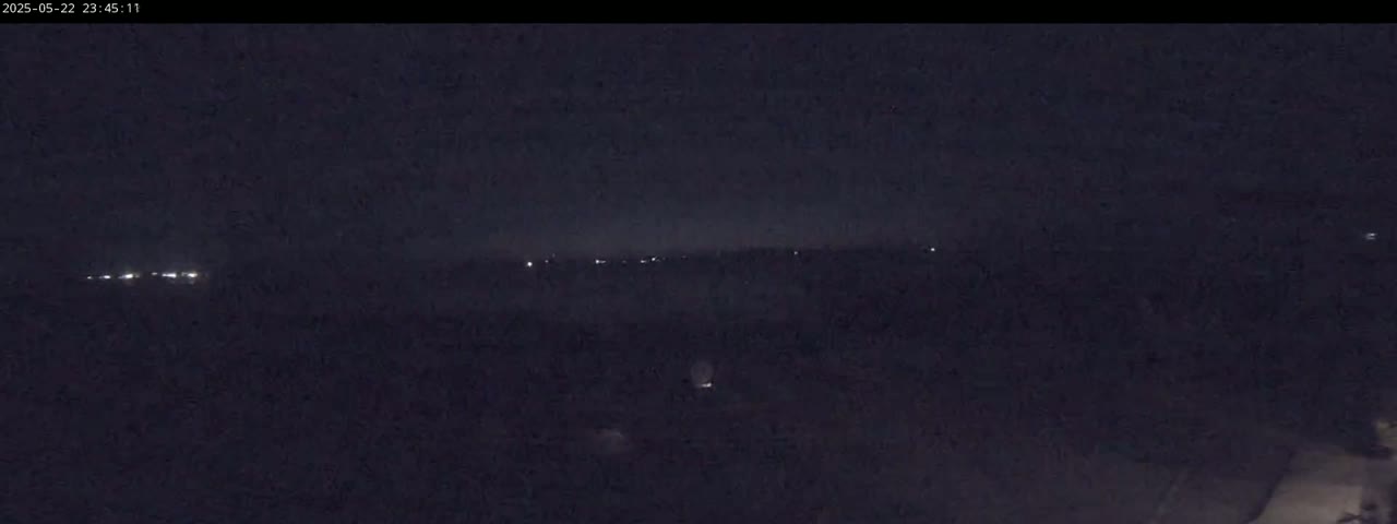 A dark, nighttime landscape shows a distant line of lights on the horizon.