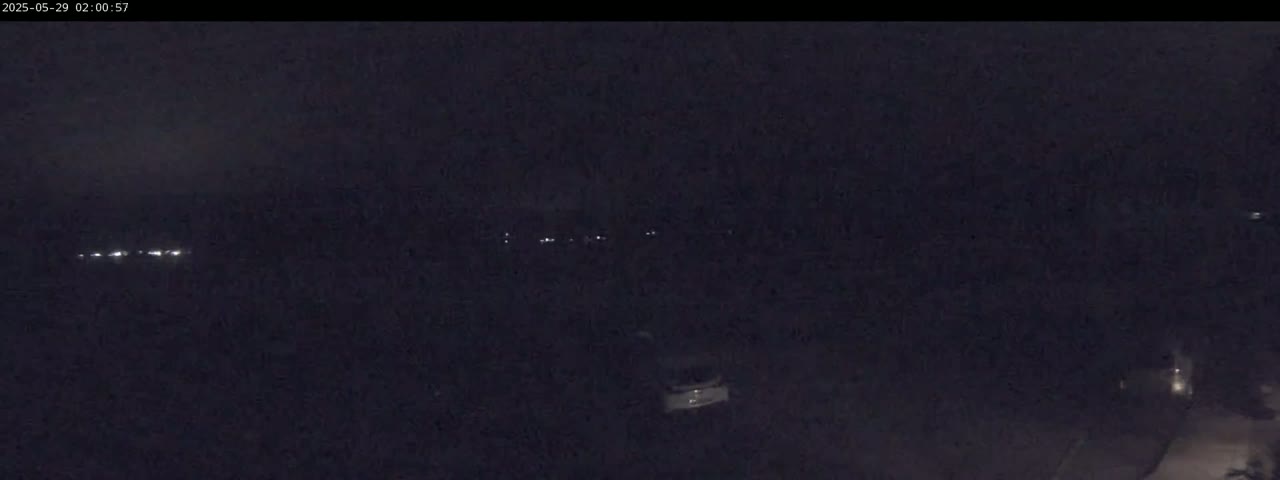 A dark, nighttime scene shows a line of distant lights, possibly vehicles, and a few faint lights closer to the viewer.