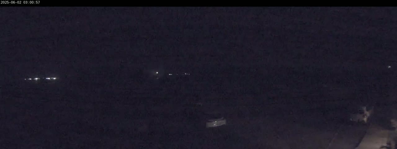 A dark, nighttime scene shows a few faint lights in the distance, possibly from vehicles or buildings, under a cloudy or overcast sky.