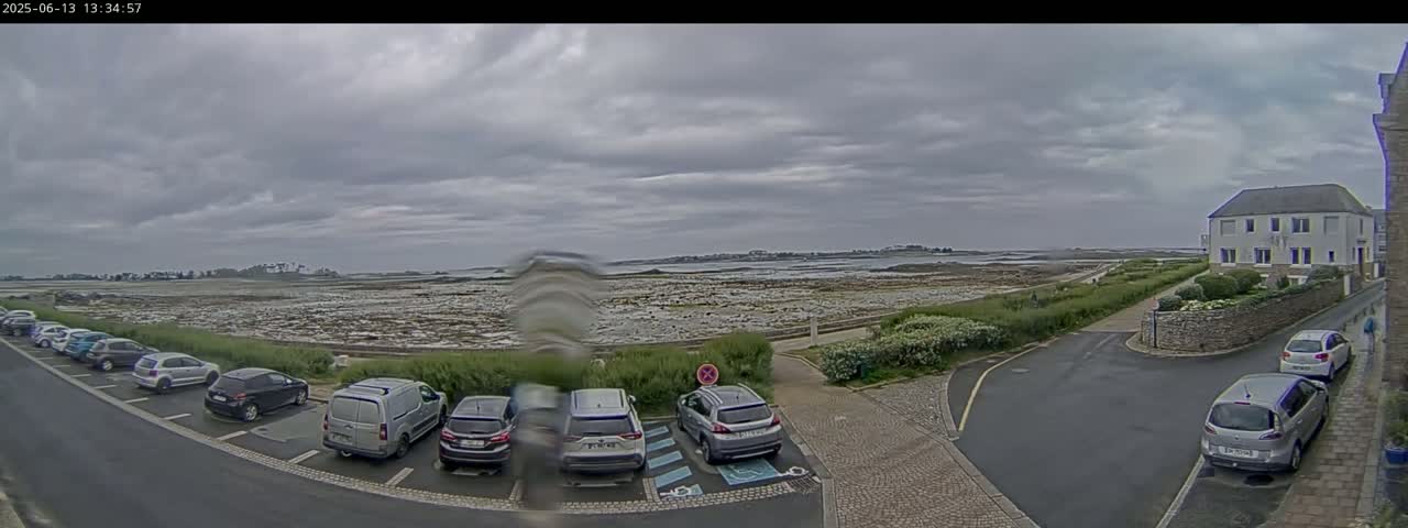 A parking lot with several cars is situated near a coastal area under an overcast sky.