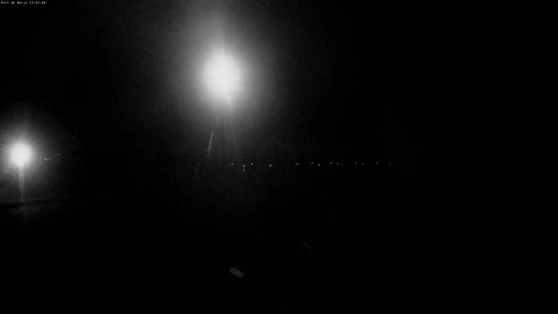 A nighttime scene shows a bright light in the center and dimmer lights in the distance, under dark, clear skies.