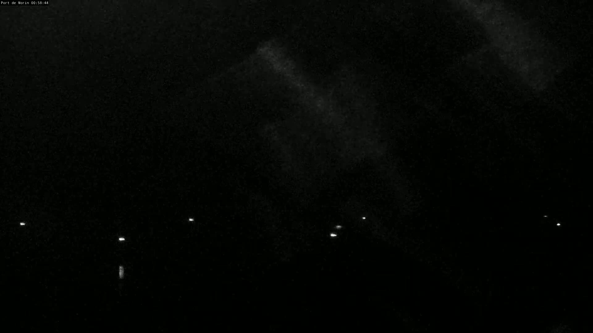 A nighttime, dark sky with faint cloud cover and a few distant lights visible on the horizon.