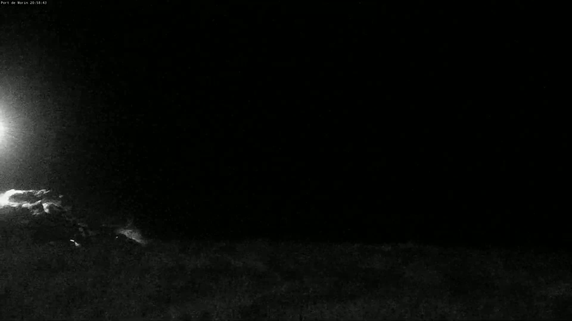 A nighttime, low-light image shows a dark, possibly grassy landscape under a mostly clear sky with a bright light source in the upper left corner.