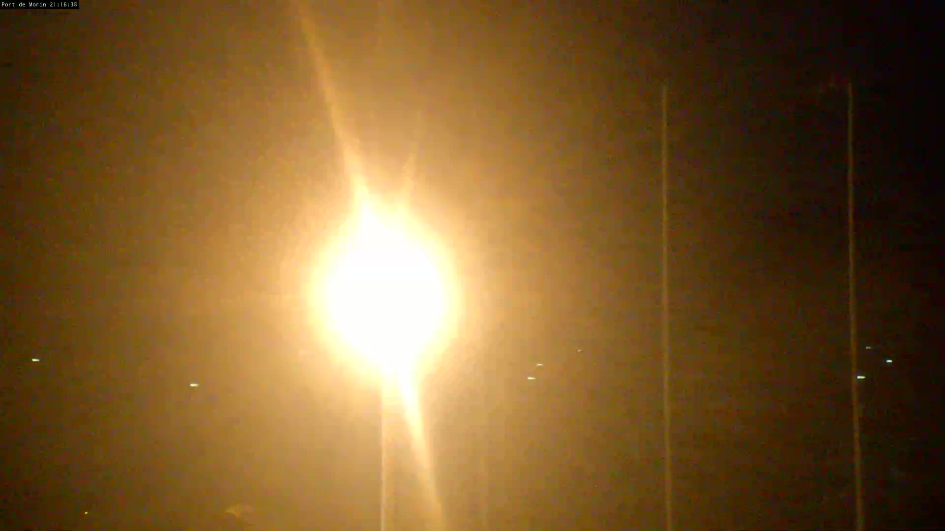A bright light shines in the night, illuminating a hazy, dark orange-brown sky.