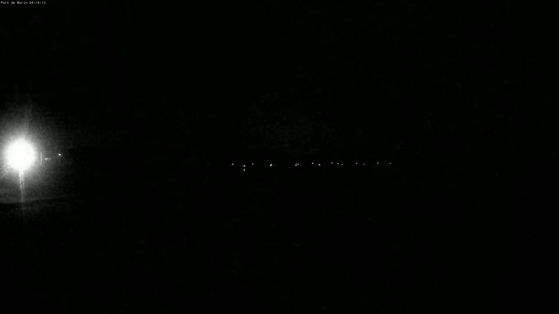 A bright light illuminates the foreground of a nighttime scene, with a line of faint lights visible in the distance under a dark sky.