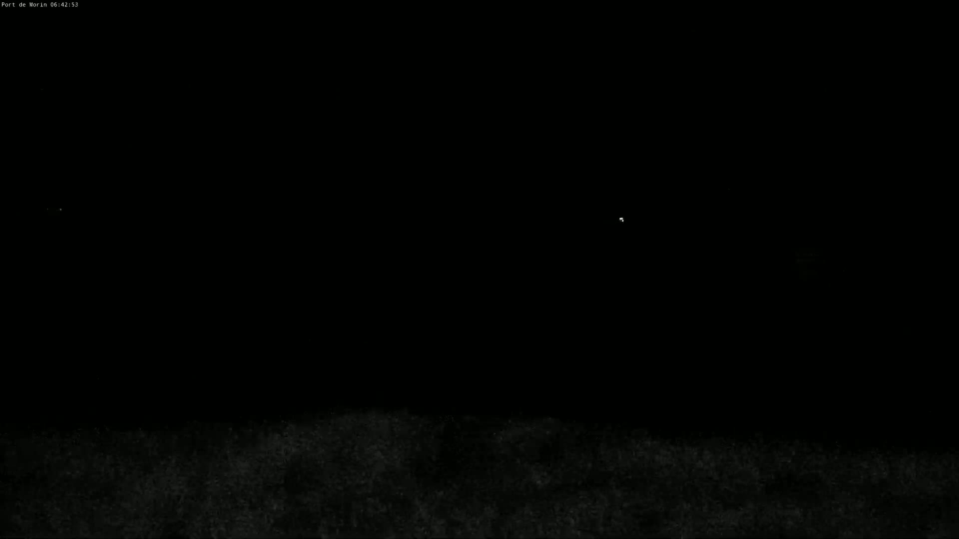 A dark, nighttime scene shows a low horizon line with faint, indistinct land or vegetation below and a few very small, distant lights in the dark sky.