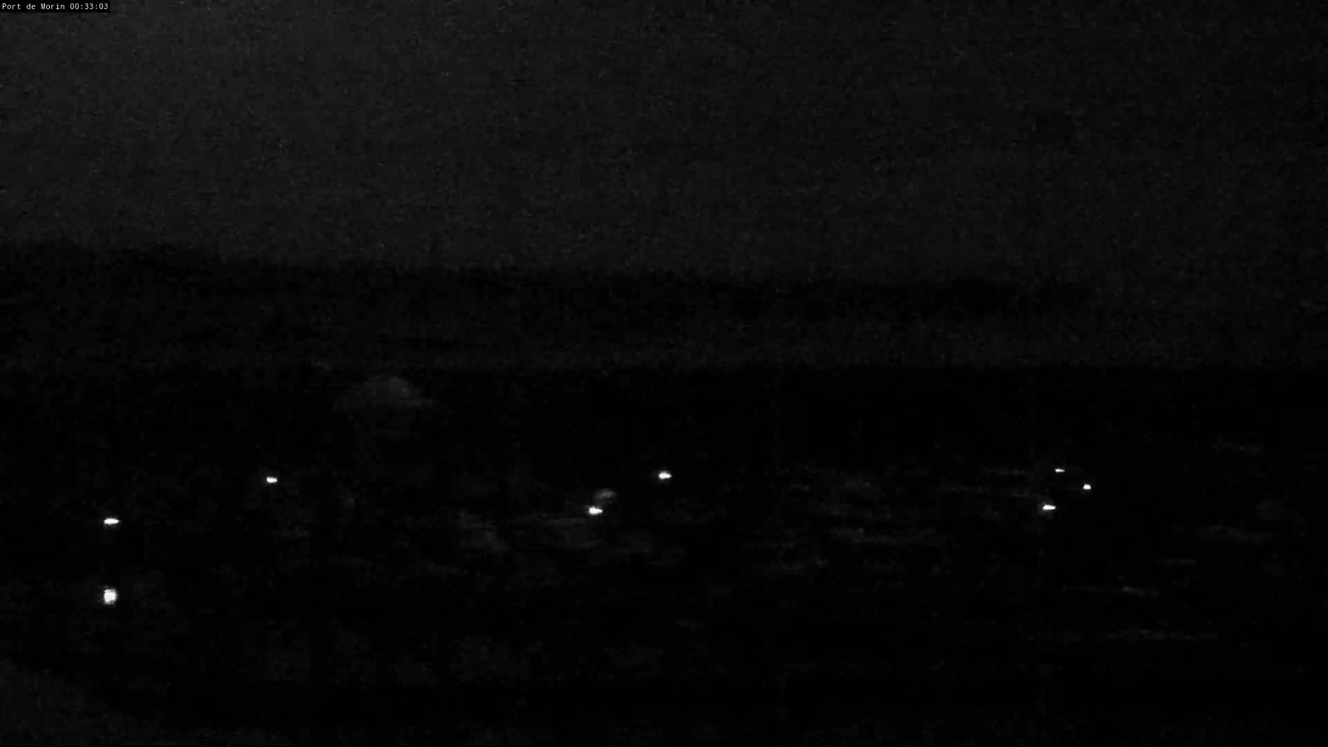 A dark, nighttime scene shows several small, bright lights scattered across a low-lying, dark area.