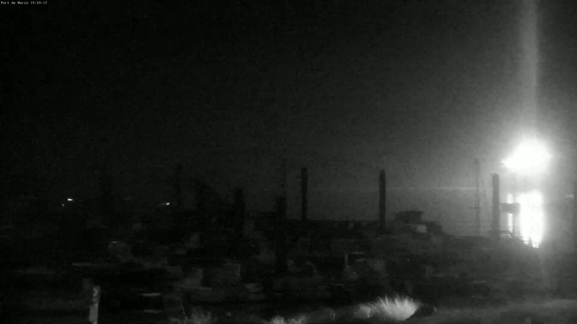 A nighttime, hazy view shows a dark industrial area with tall structures and bright lights in the distance.