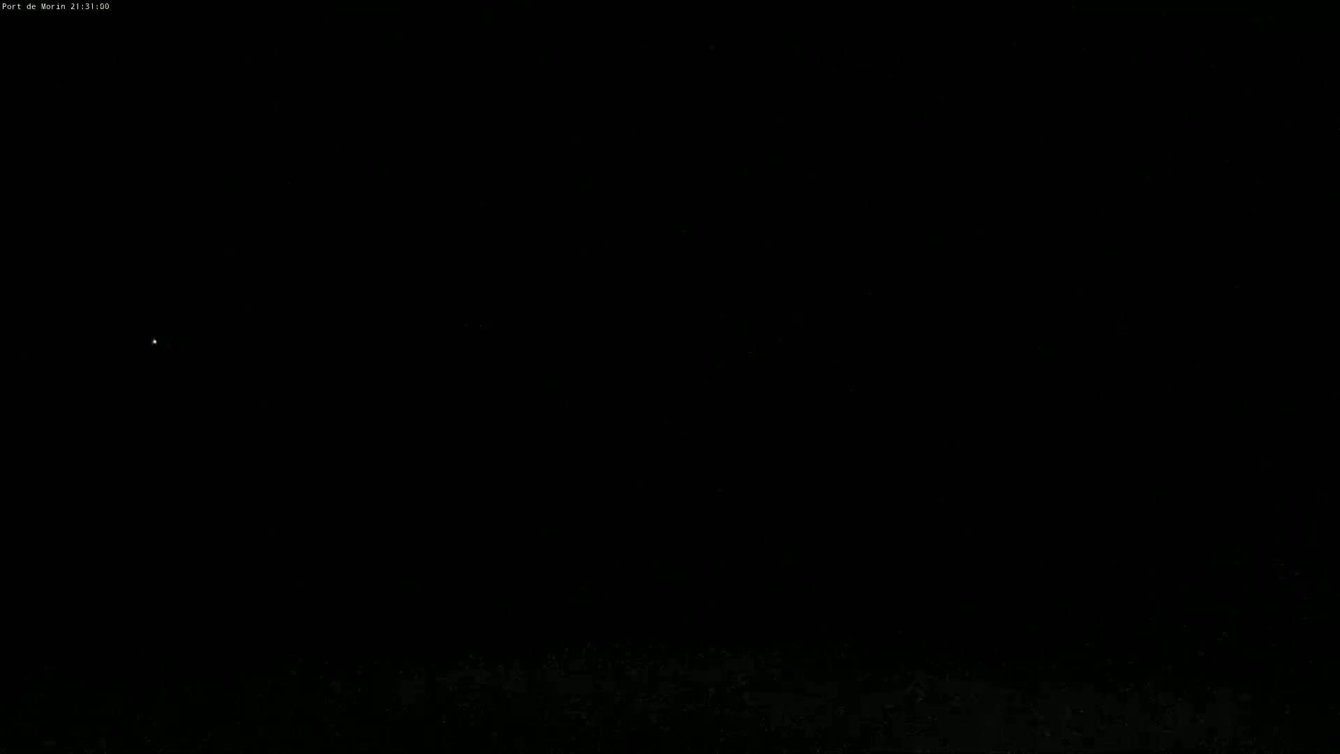 A single, faint light is visible in a dark, nighttime sky above a dark ground.