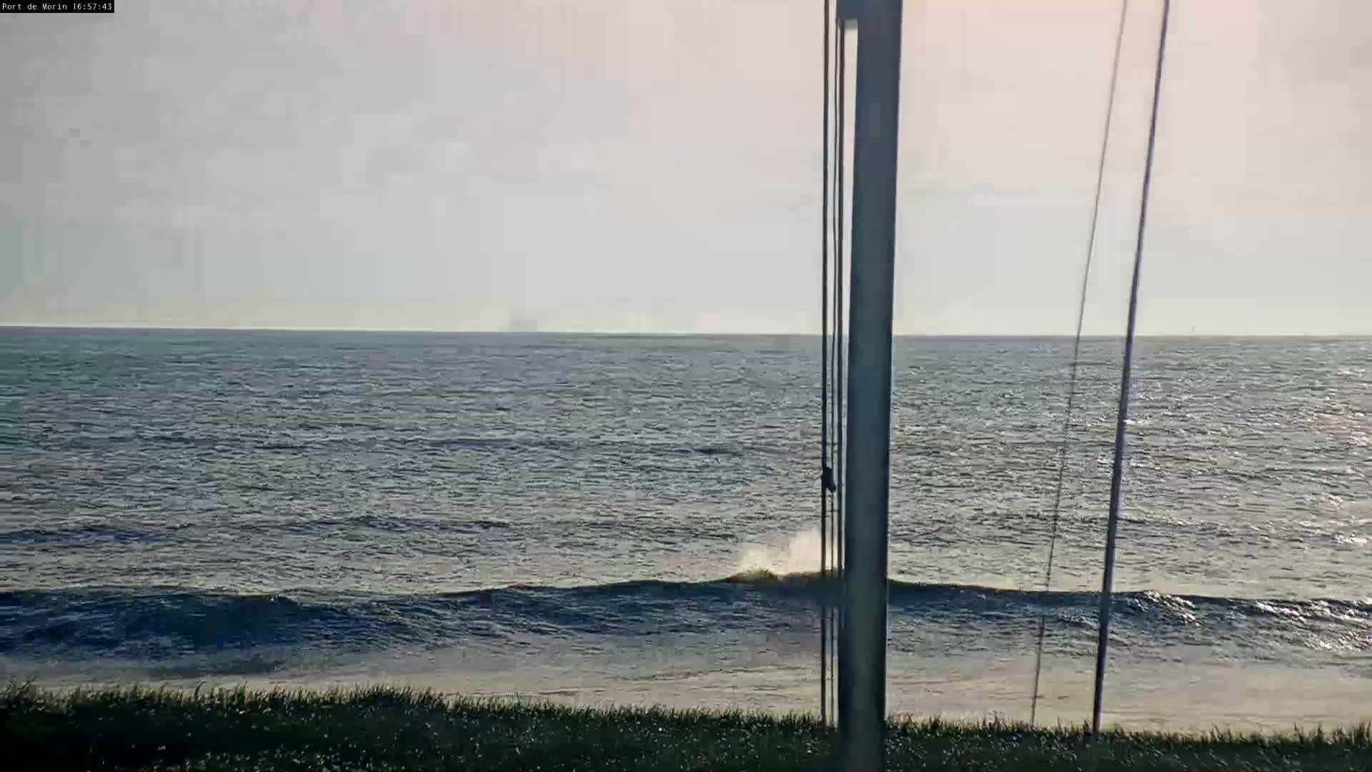 A calm ocean with small waves laps a sandy shore under a mostly clear sky.