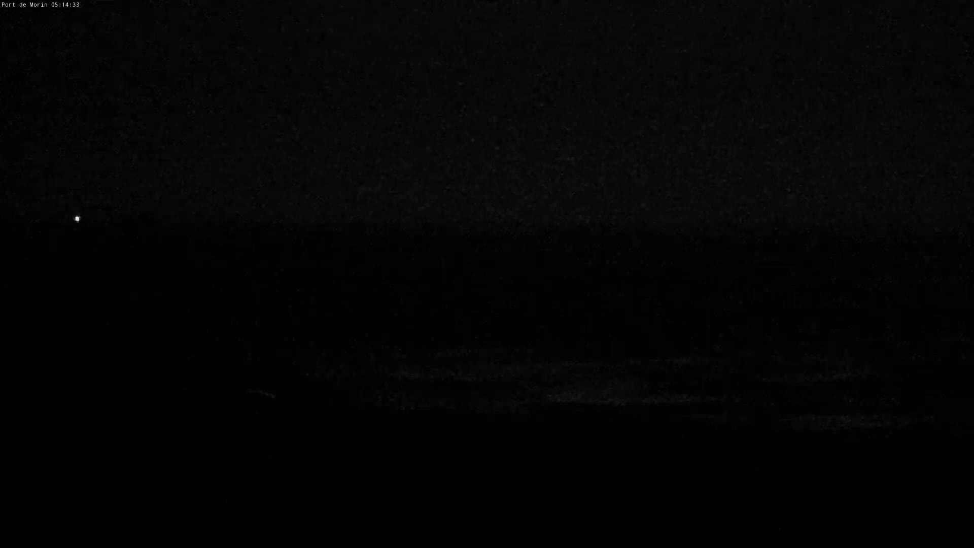 A dark, nighttime scene shows a mostly black body of water with a faint light source in the distance.