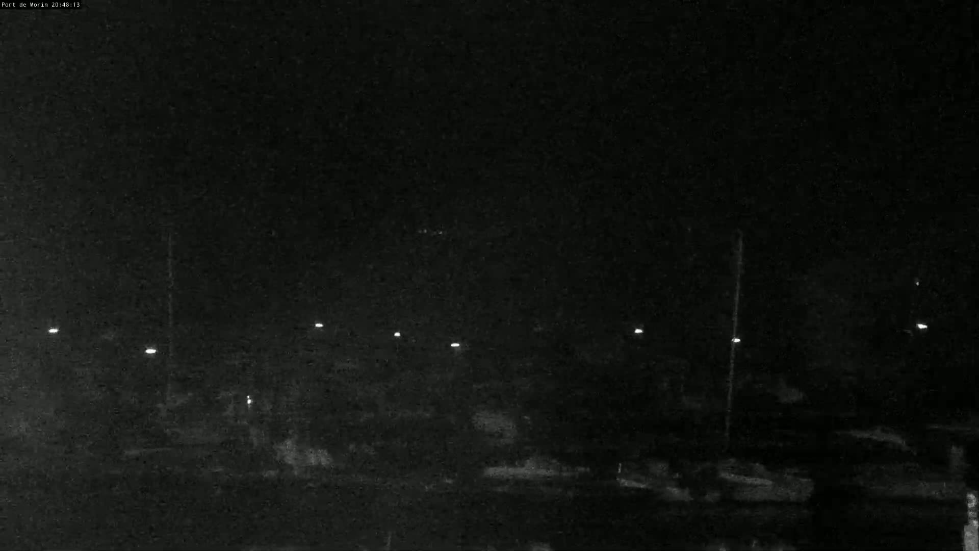 A nighttime, low-light image shows a dark landscape with several faint lights illuminating a seemingly empty area.