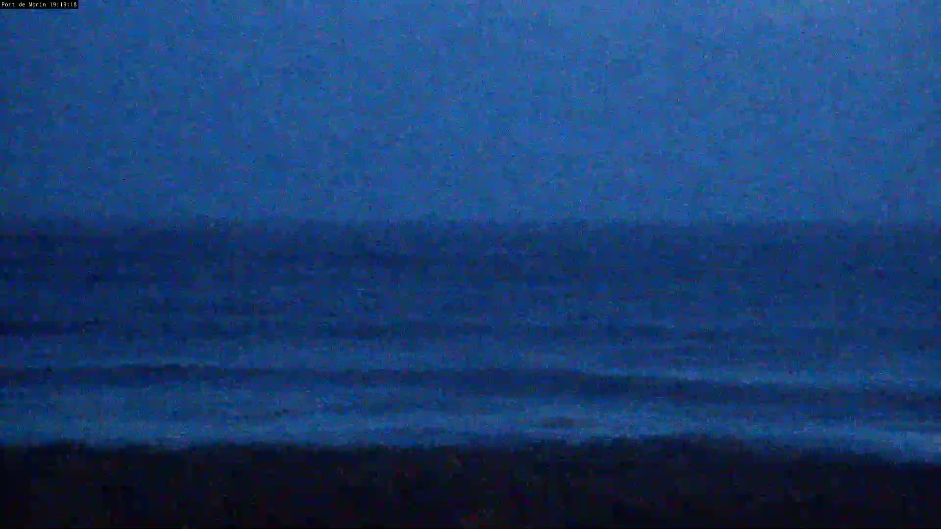A dark blue ocean with small waves rolls towards a dark shoreline under a twilight sky.