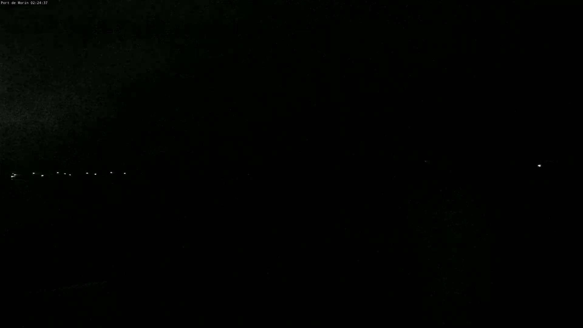 A dark, nighttime scene shows a line of faint lights in the distance.