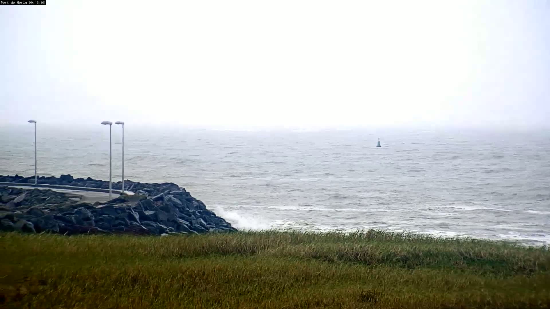 A rocky shoreline with three lampposts is visible, overlooking a choppy sea on an overcast day.