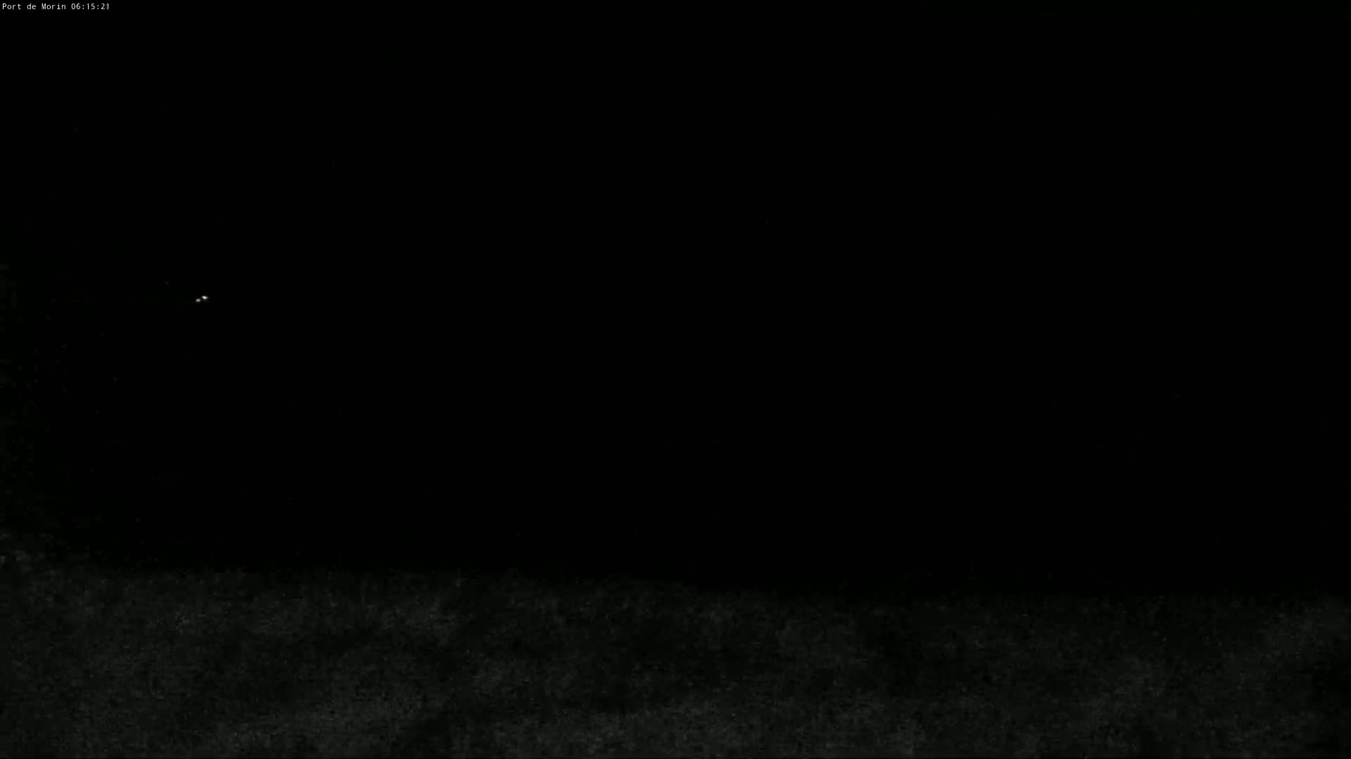 A dark, nighttime scene shows a few faint lights in the distance above a dark, textured ground.