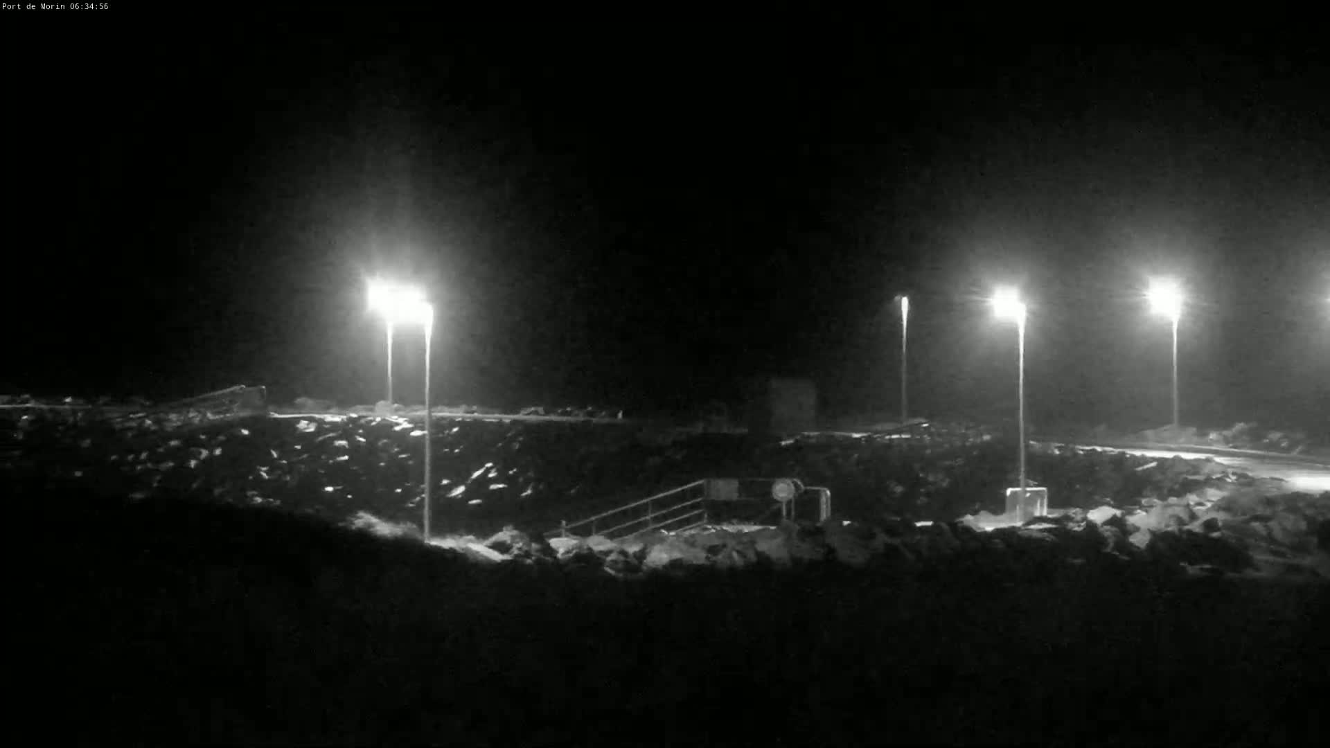 A nighttime view of a rocky area illuminated by several tall lights, possibly a harbor or waterfront at night with some snow on the ground.