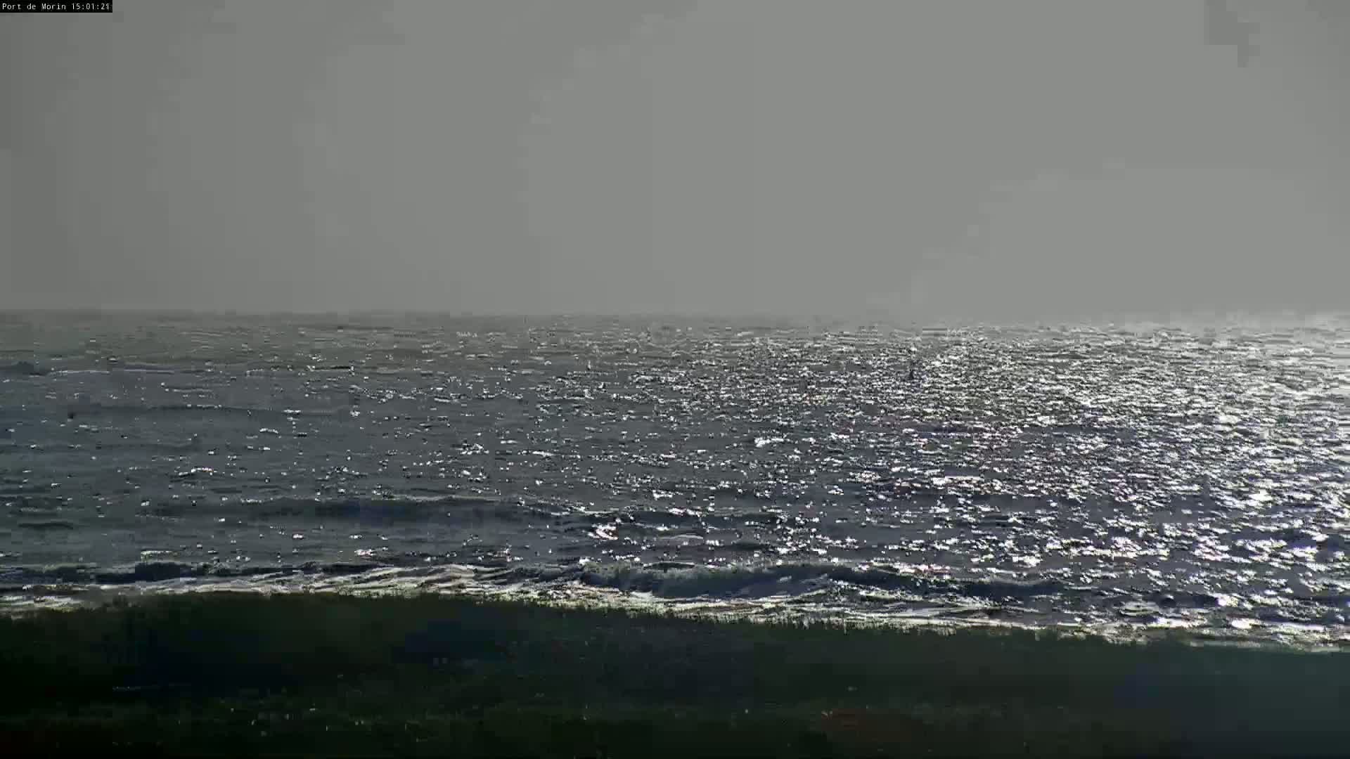 A dark, choppy sea under a hazy sky meets a dark shoreline.