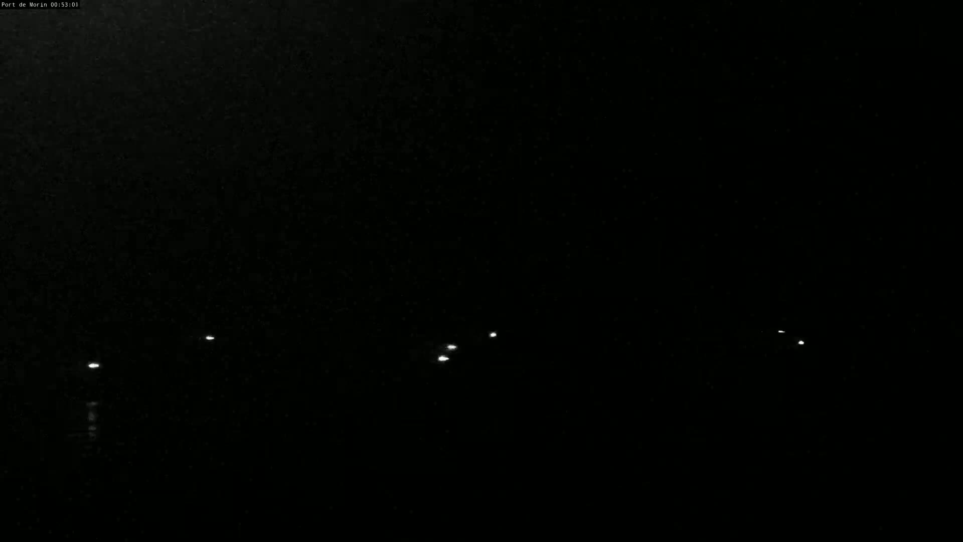 A nighttime view of several small, distant lights reflecting on dark water under a black sky.