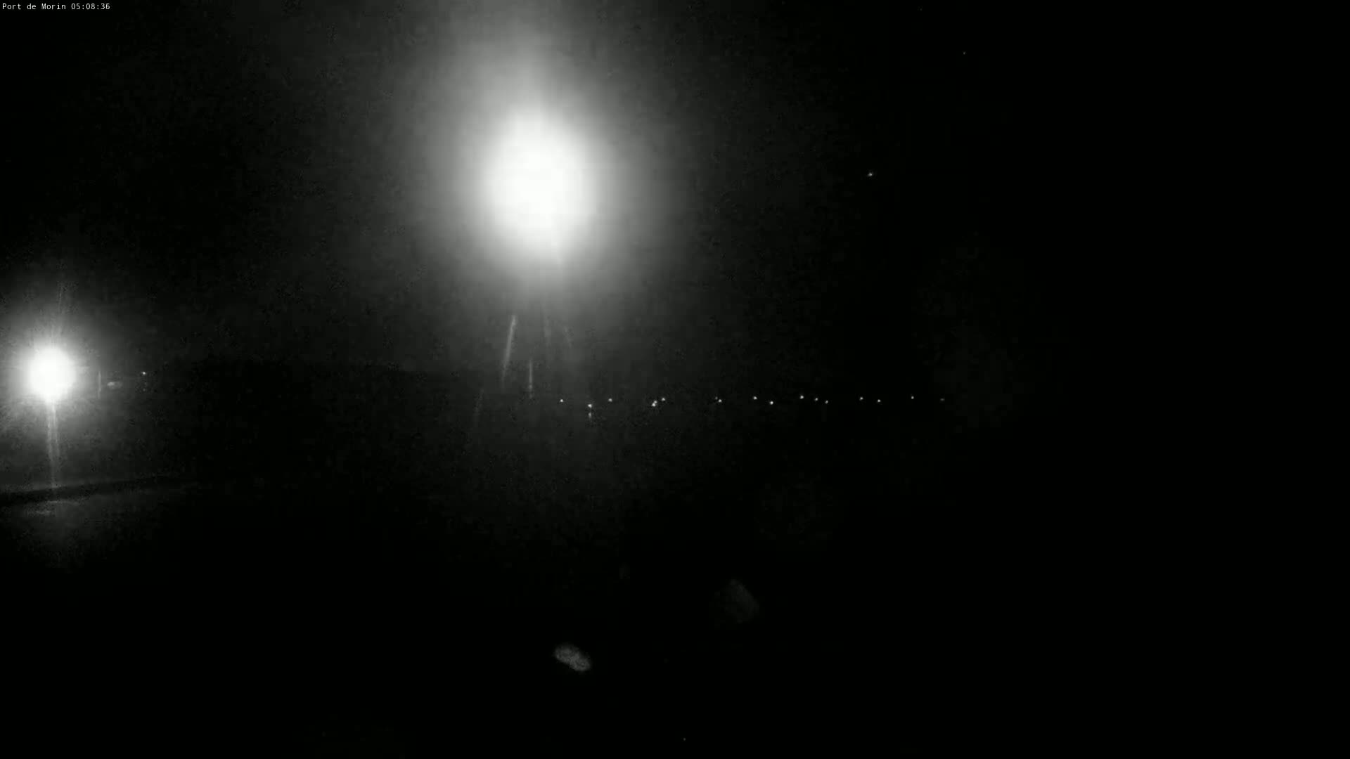 A nighttime scene shows a bright light source and a line of smaller lights in the distance under a dark sky.