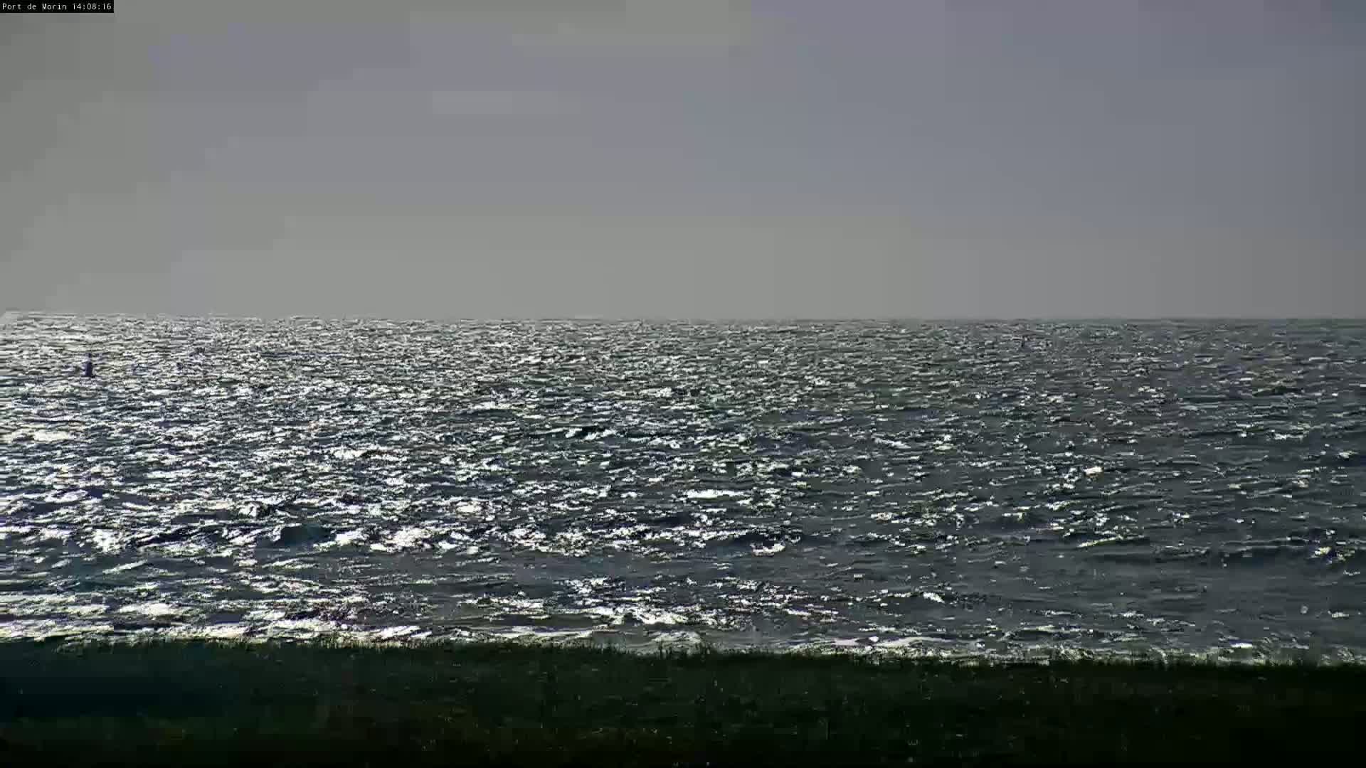 A mostly cloudy day shows a dark, choppy sea meeting a low, dark shoreline.