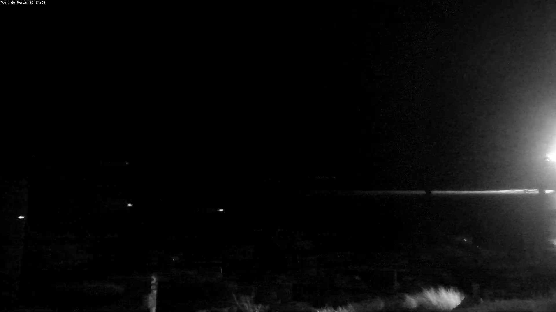 A dark, nighttime scene shows a flat expanse of land with a few faint lights visible in the distance.