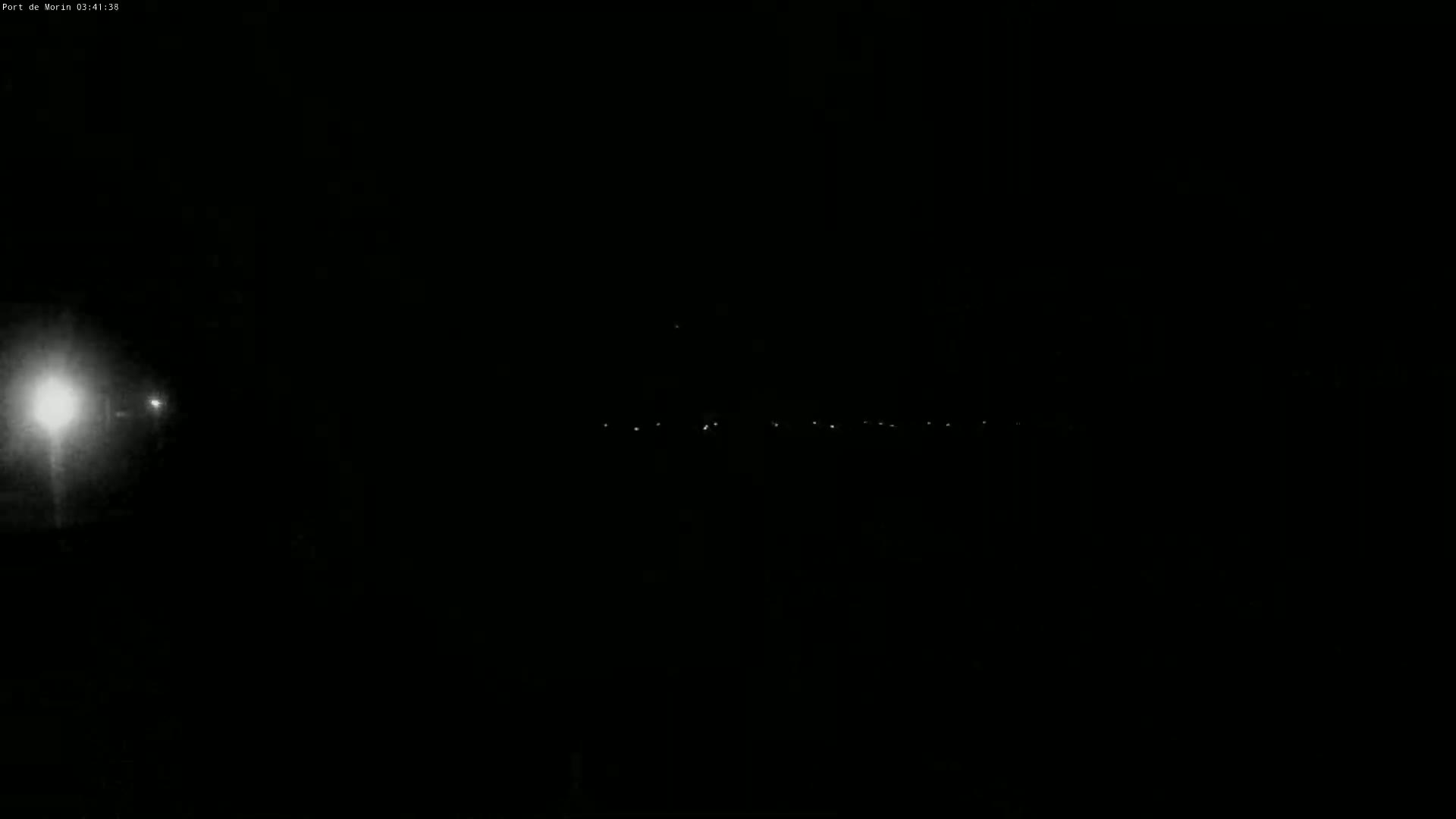 A nighttime image shows a few distant lights on a dark horizon, with a bright light source closer to the camera on the left.
