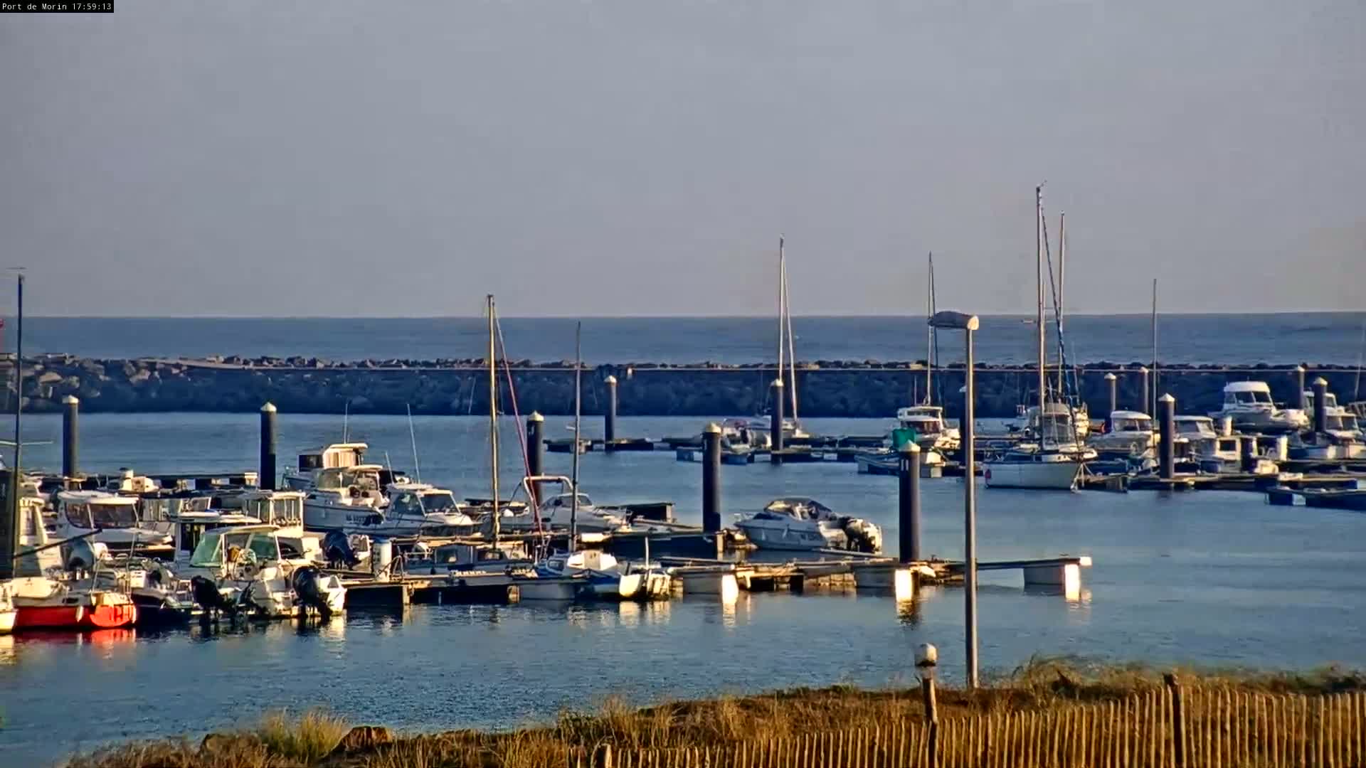 Many boats are docked in a calm harbor on a clear, sunny day.