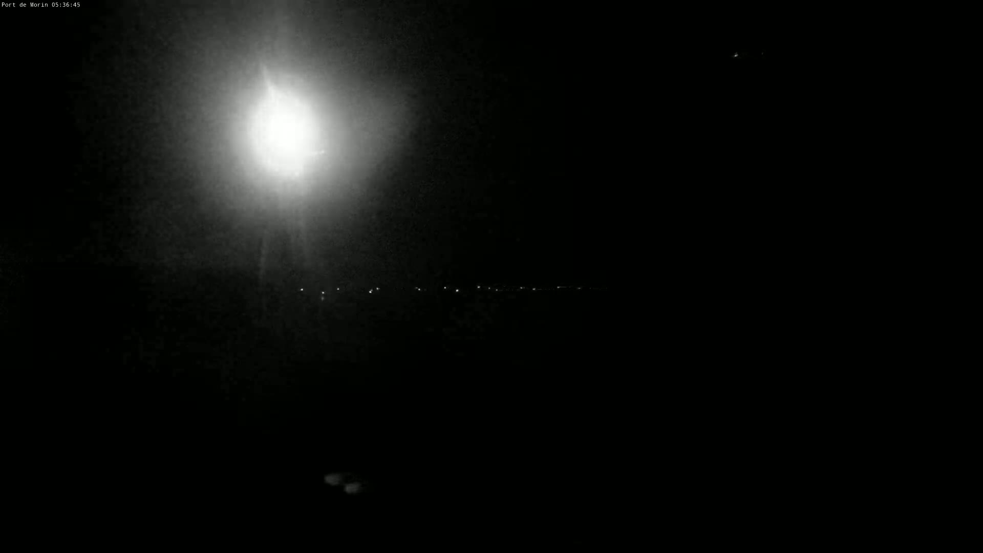 A bright light illuminates a dark, nighttime scene with a distant line of faint lights.