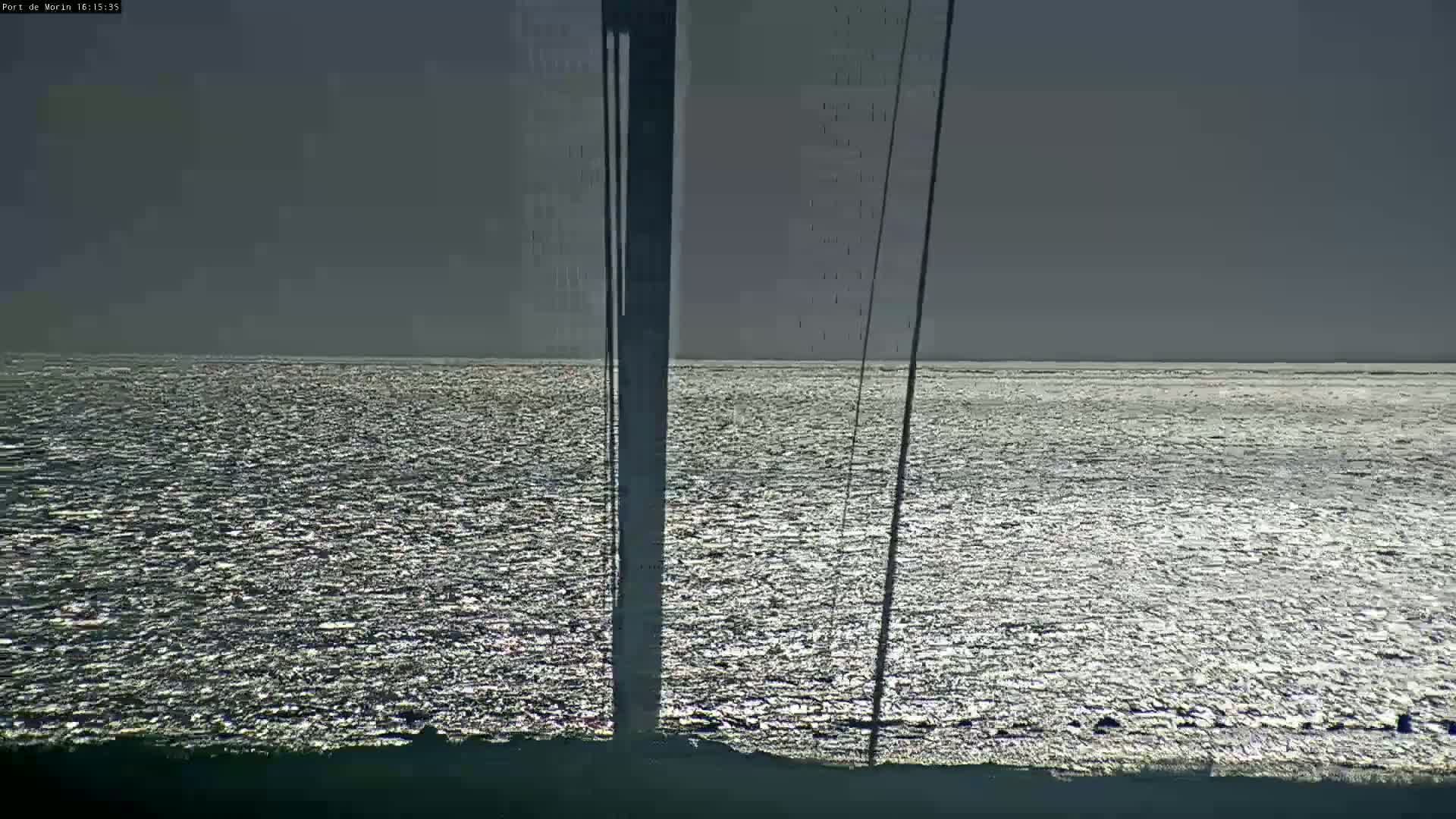 A mostly cloudy sky overlooks a shimmering body of water, partially obscured by a tall, dark pole and thin wires.